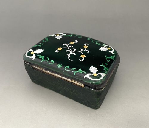fig 1. An antique dark green Georgian trinket box featuring a glass lid decorated with white, yellow, and green painted scrollwork motifs.