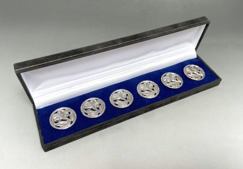 fig 1. A set of six circular sterling silver buttons with pierced floral Art Nouveau motifs displayed inside a long black velvet-lined presentation box.