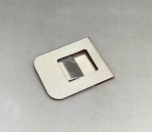 fig 1. A rectangular silver money clip featuring an engine-turned striped pattern and a central cutout spring mechanism.