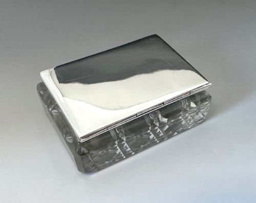 fig 1. An Edwardian rectangular cut glass stamp box topped with a smooth sterling silver lid showing hallmarks along the rim.