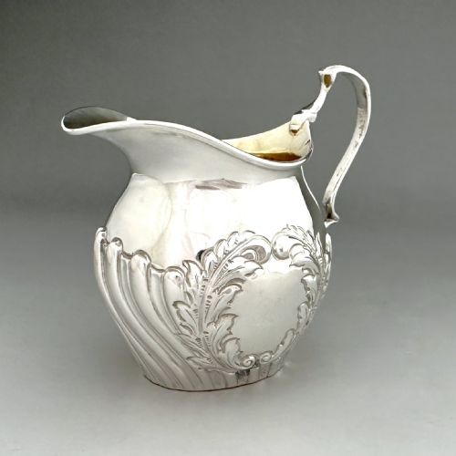 fig 1. A Victorian silver cream jug featuring chased acanthus leaf motifs, a swept scroll handle, fluted lower body, and a gilt interior.