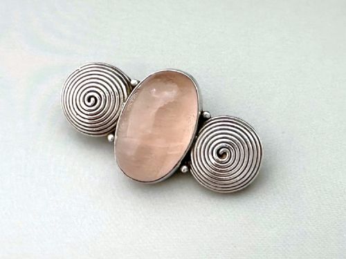 fig 1. A silver brooch featuring a central oval cabochon rose quartz flanked by two spiral silver wire motifs.