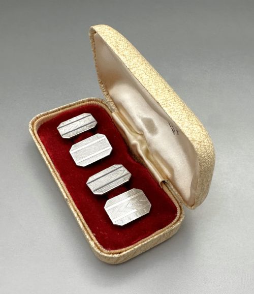 fig 1. A pair of rectangular silver cufflinks with geometric engine-turned engraving displayed inside a cream fitted presentation box with red velvet lining.