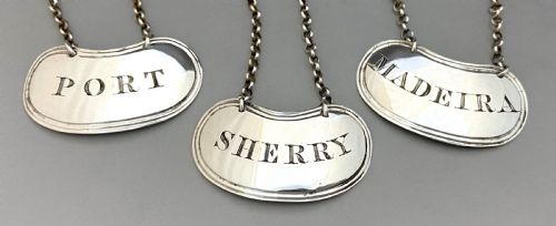 fig 1. A set of three crescent shaped sterling silver decanter labels with chains, engraved with the words Port, Sherry, and Madeira.