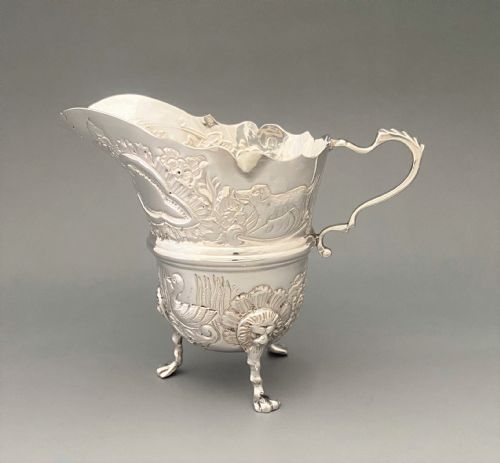 fig 1. An antique sterling silver cream jug featuring chased animal and floral motifs, a scroll handle, and three lion mask feet.