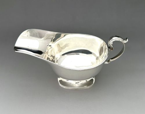 fig 1. A George V sterling silver sauce boat featuring a scroll handle, extended pouring spout, and pedestal foot base.
