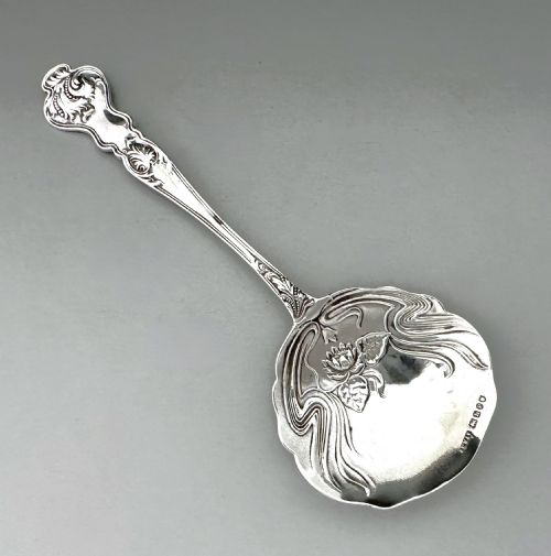 fig 1. An antique Art Nouveau sterling silver preserve spoon featuring a scalloped bowl with an embossed water lily design and a hallmarked surface.