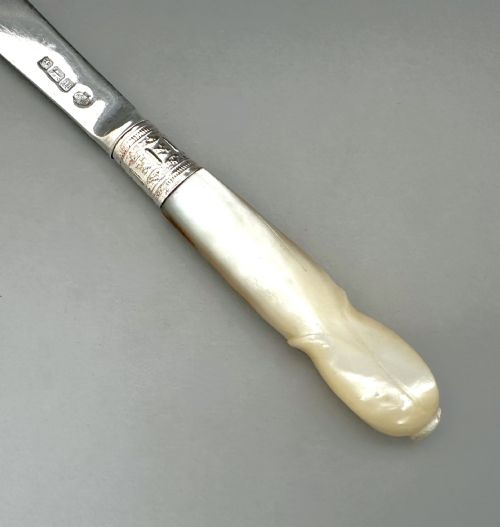 fig 1. An antique George V letter opener featuring a tapered silver blade, an engraved silver collar, and a carved mother-of-pearl handle.