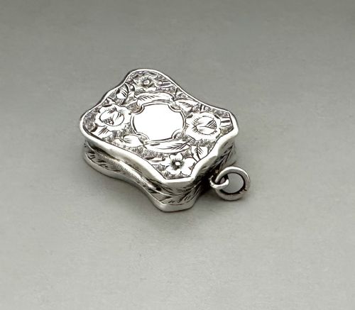 fig 1. A shaped Victorian sterling silver vinaigrette with hand-engraved floral foliage, a central unengraved cartouche, and a side suspension ring.