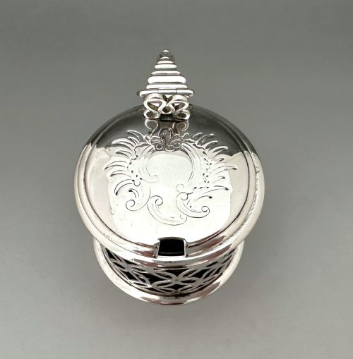 fig 2. A William IV sterling silver drum mustard pot featuring openwork geometric fretwork, a fitted blue glass liner, an engraved flat lid with a thumbpiece, a scroll handle, and a silver spoon.