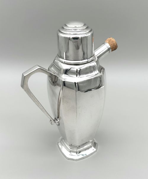 fig 1. A polished silver-plated Art Deco cocktail shaker featuring an angular handle, stepped lid cap, and cork-capped spout.