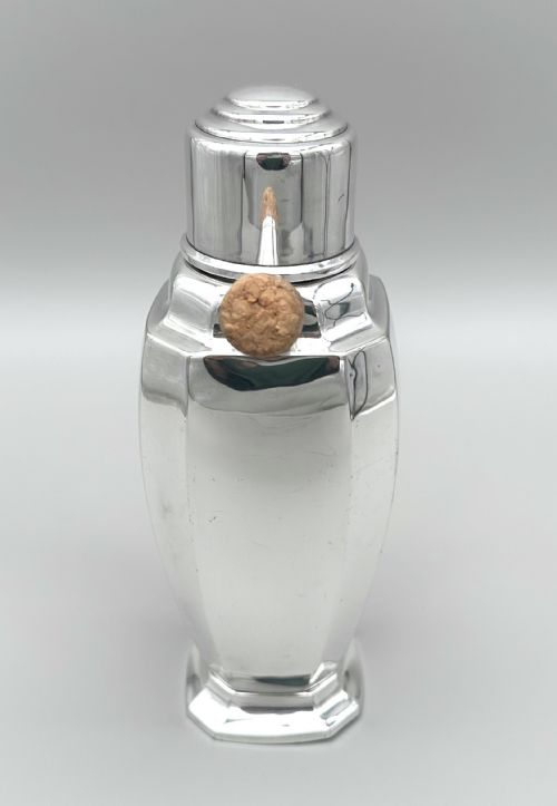 fig 2. A polished silver-plated Art Deco cocktail shaker featuring an angular handle, stepped lid cap, and cork-capped spout.