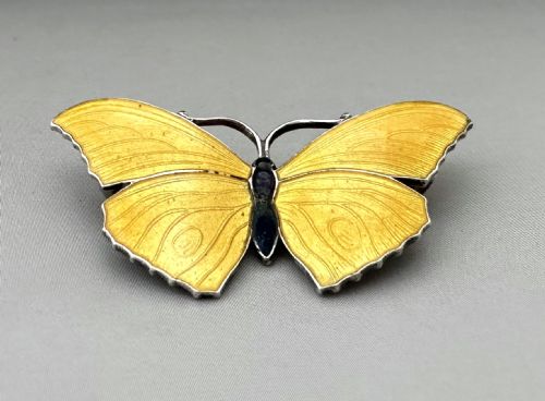 fig 1. A silver butterfly brooch featuring yellow guilloche enamel wings and a dark central body.