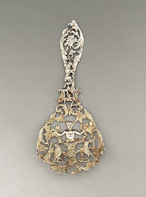 fig 1. An ornate Victorian cast sterling silver bonbon spoon featuring intricate pierced scrollwork, foliage, and a cherub motif.