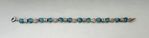 fig 1. A silver filigree link bracelet featuring bow-shaped segments filled with turquoise blue enamel and secured with a bolt ring clasp.