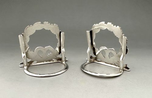 fig 1. A pair of sterling silver menu card holders shaped as laurel and oak leaf wreaths tied with a ribbon bow on a flat base with rear support struts.