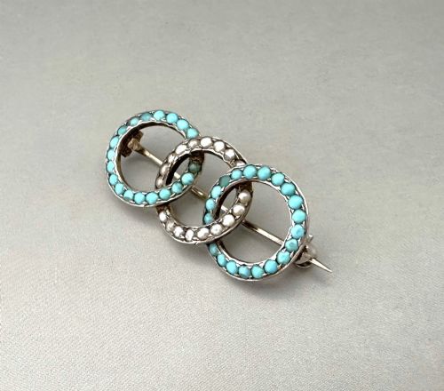 fig 1. A silver gilt horizontal brooch formed of three interlocking circular rings set with turquoise cabochons and split seed pearls.