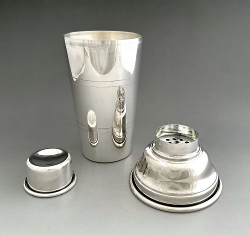 fig 1. A polished silver-plated three-piece Art Deco cocktail shaker featuring a tapered cylindrical body with incised lines and a stepped cap.