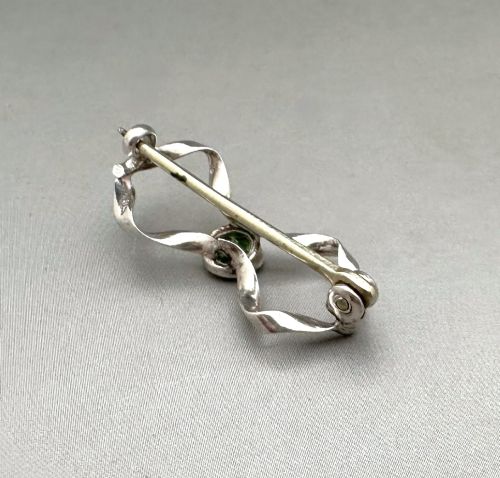 fig 1. An Edwardian sterling silver brooch styled as a ribbon bow with a faceted green peridot stone set in the centre.