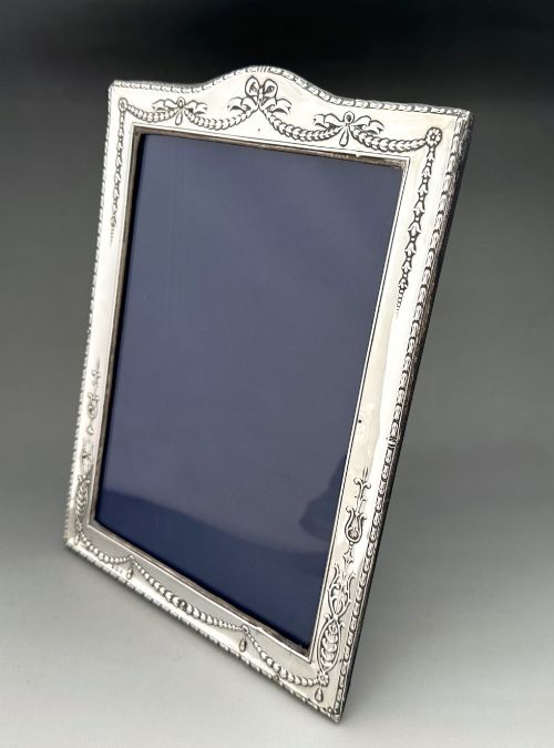 fig 1. An Edwardian sterling silver portrait photo frame featuring embossed ribbon, garland, and swag decorative motifs with an arched top.