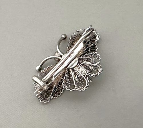 fig 1. A sterling silver filigree brooch shaped like a butterfly with detailed openwork lace wings, textured body, and ball-tipped antennae.