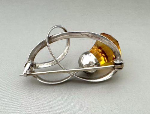 fig 1. An Edwardian silver brooch designed in an openwork loop motif featuring a stylized Scottish thistle set with a faceted amber-coloured stone.