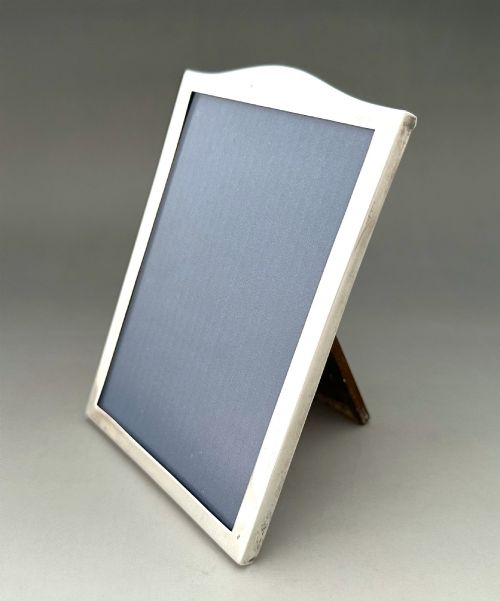 fig 1. A rectangular sterling silver photo frame featuring a gently arched top edge, hallmark stamps along the side, and a dark blue insert.