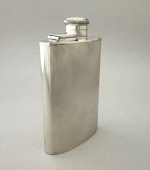 fig 1. An Art Deco silver curved hip flask featuring fine engine-turned geometric detailing and a hinged cap.
