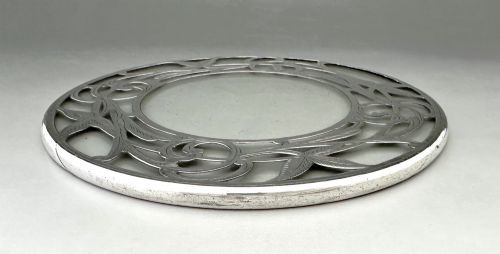 fig 1. A circular clear glass teapot stand featuring a sterling silver rim with openwork Art Nouveau leaf motifs.