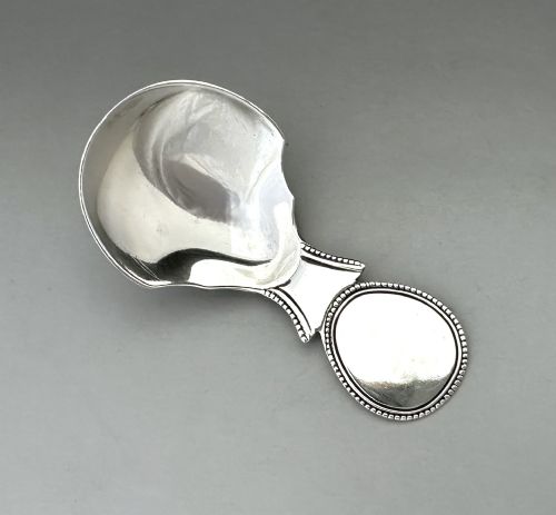 fig 1. A Regency sterling silver caddy spoon featuring a polished shovel bowl and an oval handle decorated with a beaded edge.