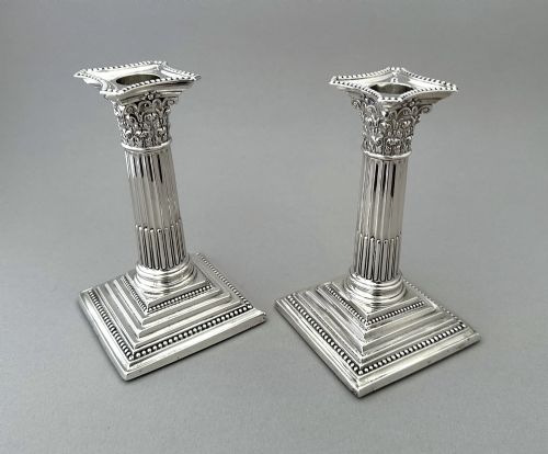 fig 2. A pair of polished silver candlesticks crafted in the form of fluted Corinthian columns with acanthus capitals and stepped square bases.