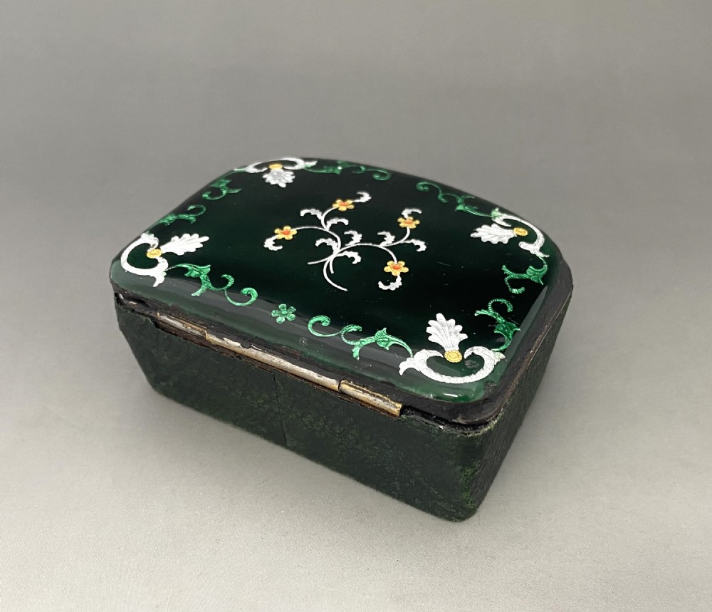 An antique dark green Georgian trinket box featuring a glass lid decorated with white, yellow, and green painted scrollwork motifs. View II