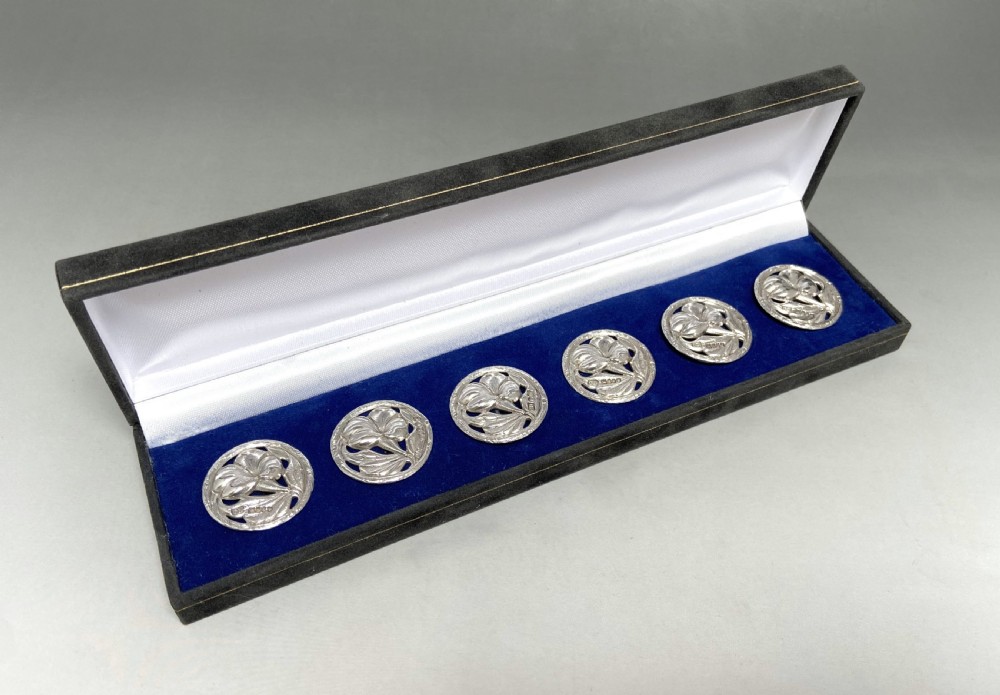 A set of six circular sterling silver buttons with pierced floral Art Nouveau motifs displayed inside a long black velvet-lined presentation box. View II