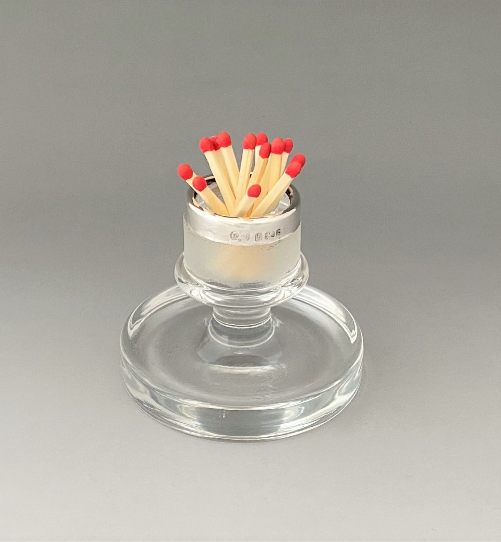 An Edwardian clear glass match striker featuring a tray base, a frosted striking column, and a hallmarked sterling silver rim holding matches.