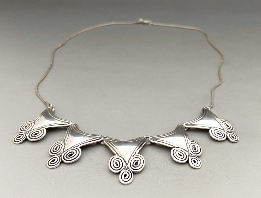 A mid-century silver necklace featuring five triangular linked panels with spiral scrollwork details suspended from a fine silver chain. View III