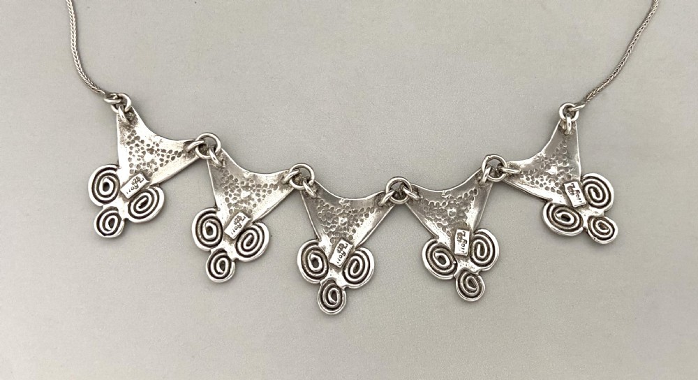 A mid-century silver necklace featuring five triangular linked panels with spiral scrollwork details suspended from a fine silver chain. View V