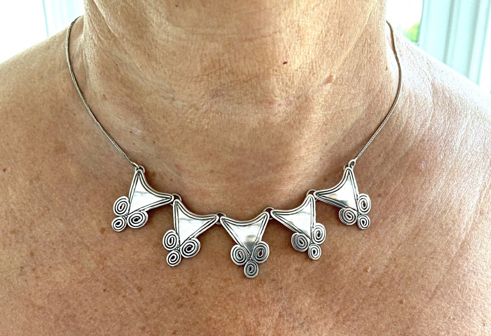 A mid-century silver necklace featuring five triangular linked panels with spiral scrollwork details suspended from a fine silver chain. View VI