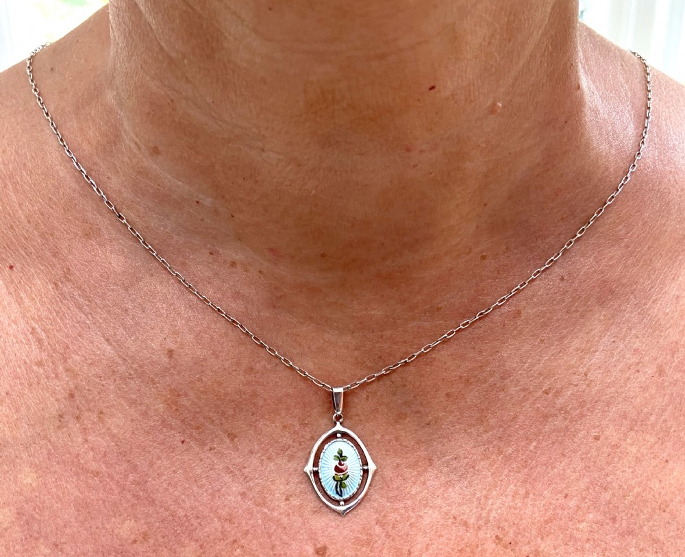 An oval sterling silver pendant displaying light blue guilloche enamel with a central floral detail within an openwork frame on a chain. View VI