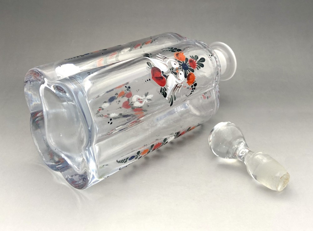 A clear glass decanter decorated with hand-painted enamel folk art motifs, featuring two white birds, a red heart, and a fitted glass stopper. View VI