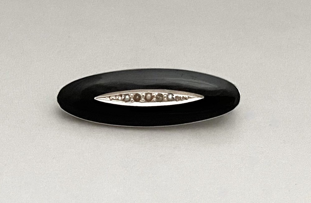 An oval black enamel silver brooch featuring a central navette-shaped aperture inset with a line of small seed pearls.