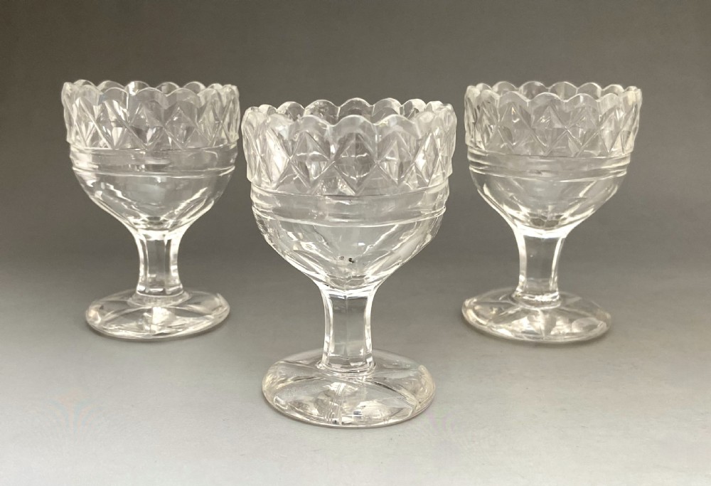 A trio of Georgian clear cut glass pedestal table salts featuring scalloped rims and diamond cutting. View V