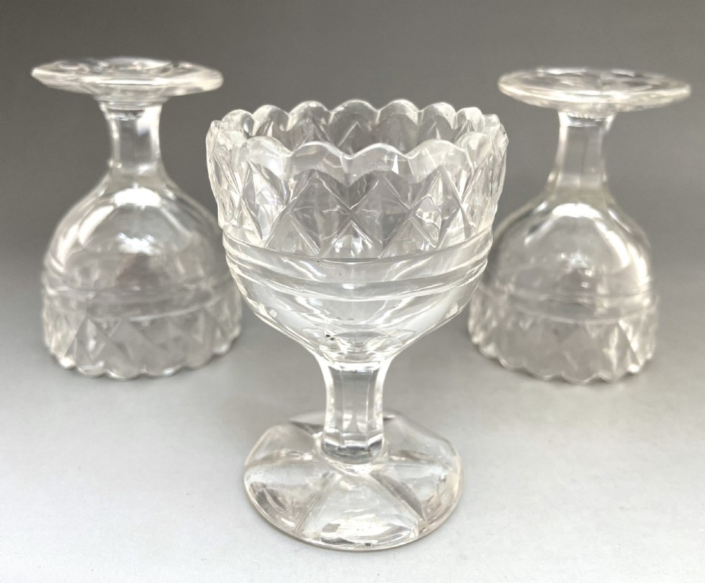 A trio of Georgian clear cut glass pedestal table salts featuring scalloped rims and diamond cutting. View VI