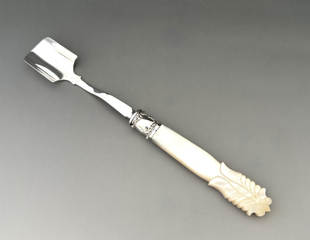 A Victorian silver Stilton scoop featuring a curved scoop blade, decorative metallic ferrule, and carved mother of pearl handle.