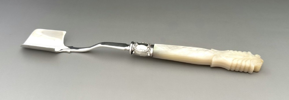 A Victorian silver Stilton scoop featuring a curved scoop blade, decorative metallic ferrule, and carved mother of pearl handle. View V