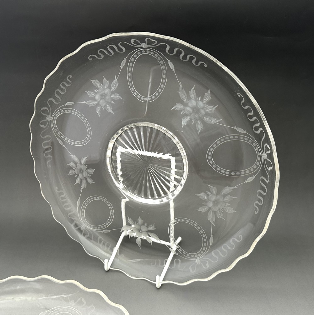 A pair of clear Edwardian glass plates featuring etched floral garlands, scalloped rims, and starburst cut centres. View III