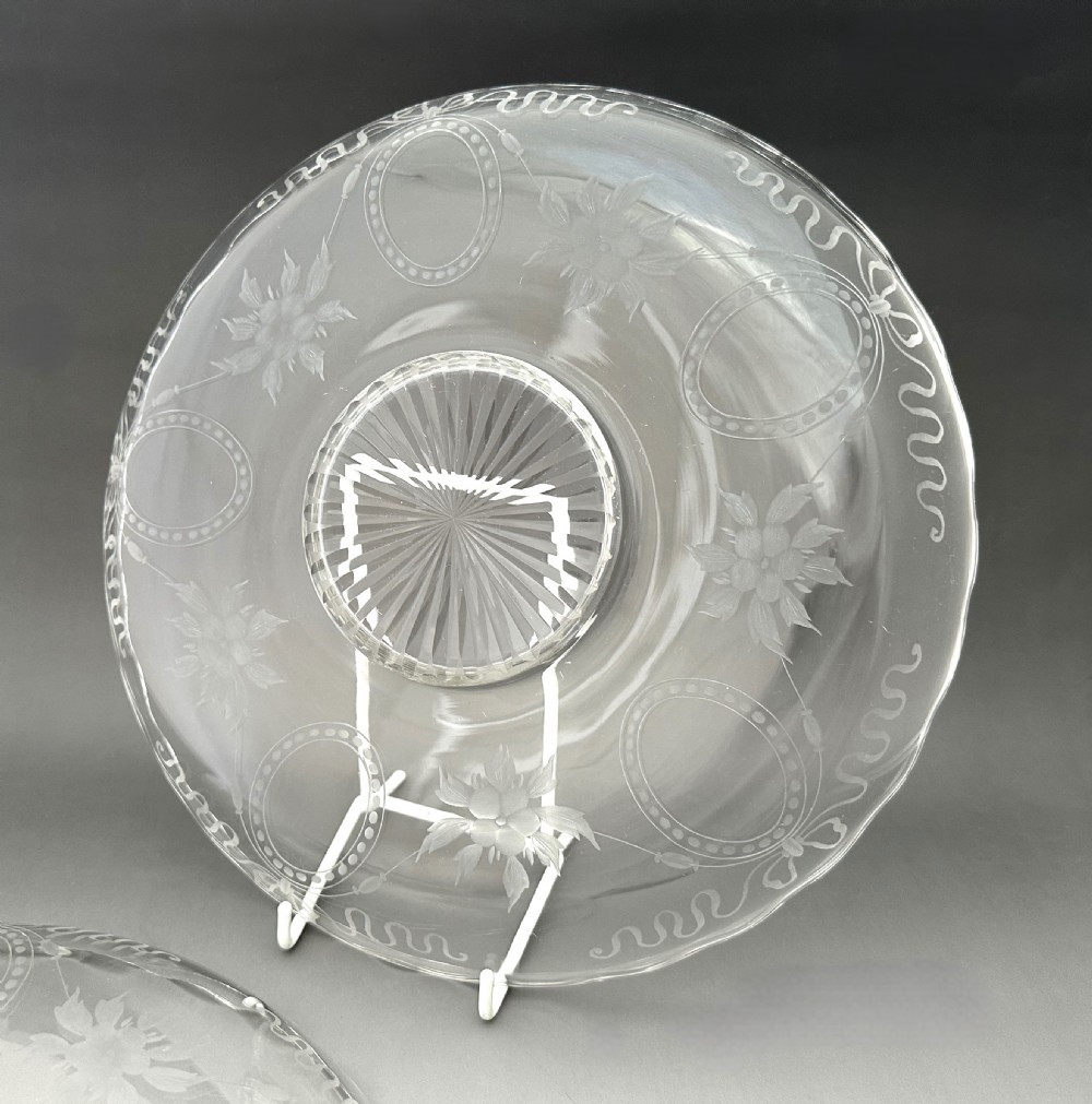 A pair of clear Edwardian glass plates featuring etched floral garlands, scalloped rims, and starburst cut centres. View V