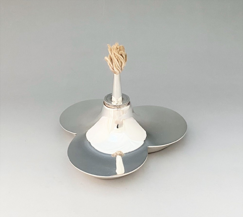 A polished silver table lighter featuring a three-lobed trefoil base and a central upright nozzle holding a thick cotton wick.