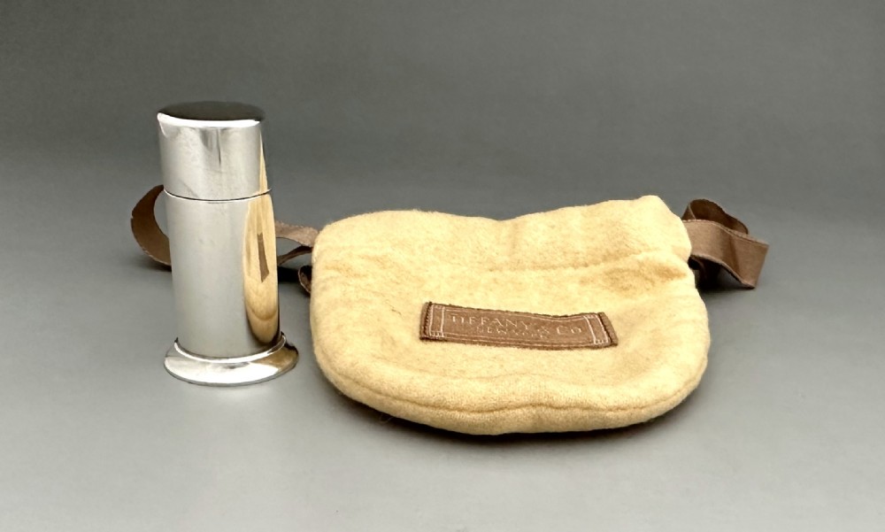A polished cylindrical sterling silver stamp moistener shown next to its original fabric storage pouch.