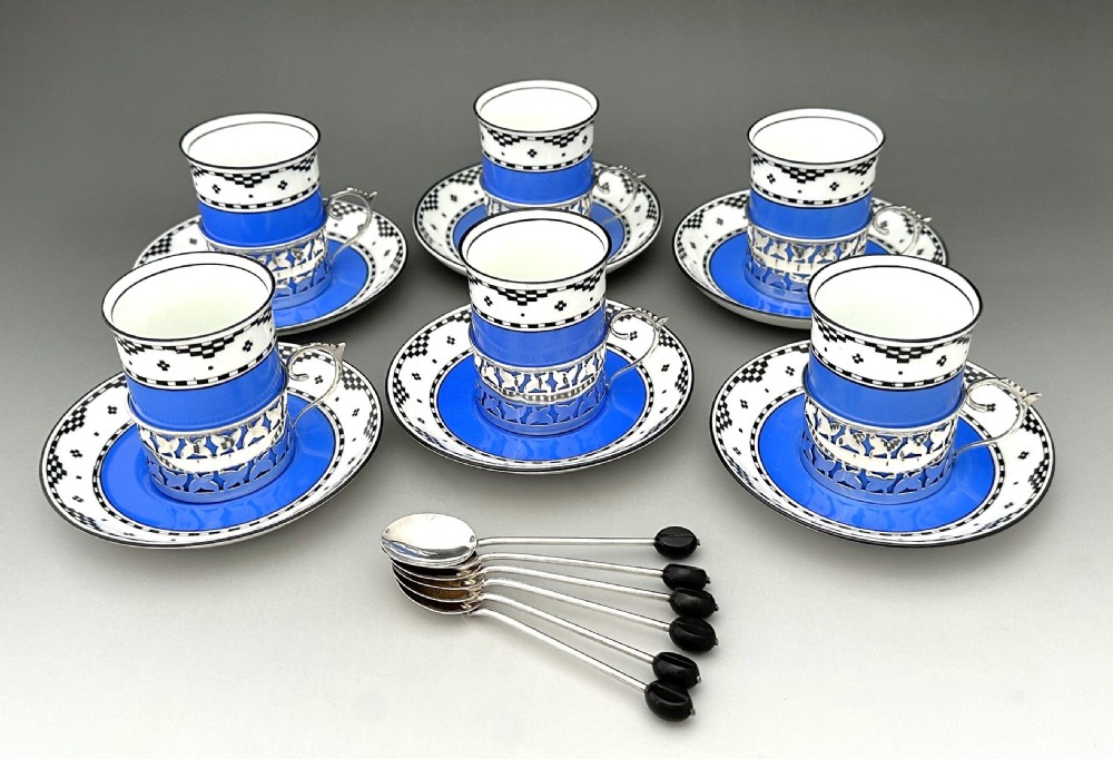 A set of six Art Deco blue porcelain coffee cans featuring pierced sterling silver mounts, matching saucers, and silver spoons with black coffee bean finials.