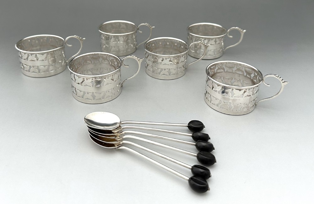 A set of six Art Deco blue porcelain coffee cans featuring pierced sterling silver mounts, matching saucers, and silver spoons with black coffee bean finials. View IX